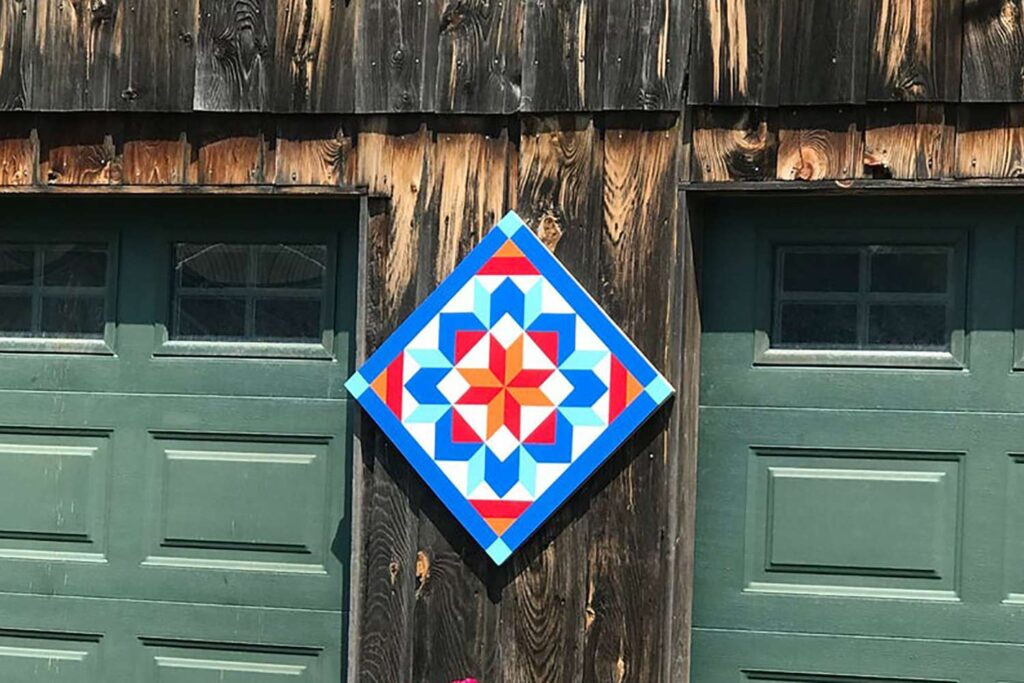 a colorful patterned barn quilt hanging on the wooden pole.