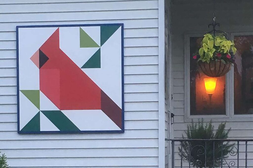 a barn quilt with a pattern of a red bird hanging on the wall next to the balcony.