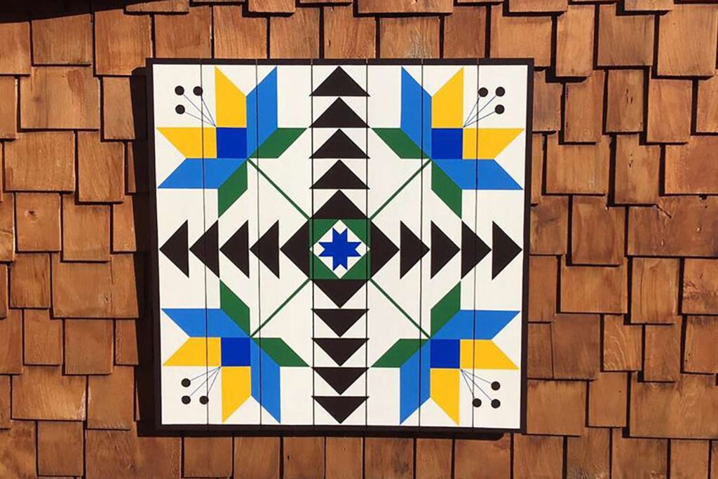 a barn quilt with a pattern of 4 flowers hanging on a wooden wall.