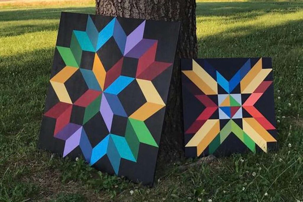 2 barn quilts leaning against a tree.