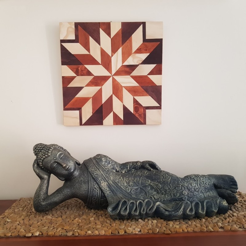 a barn quilt hanging on the wall, above a home decor buddha statue.