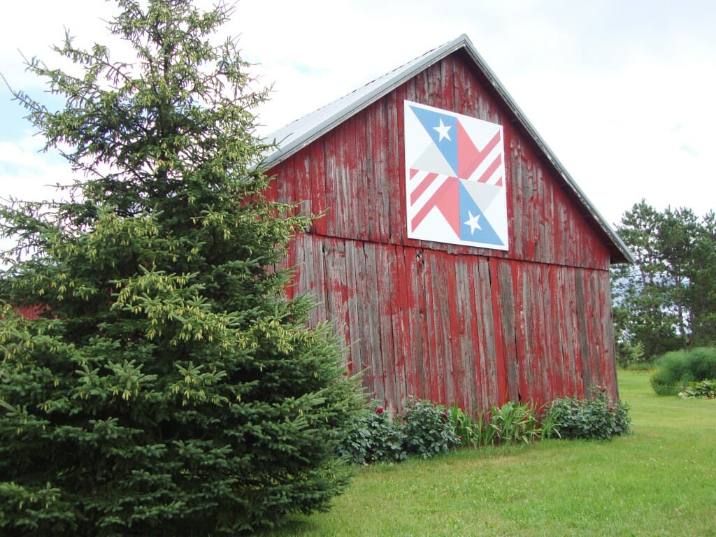 a barn quilt with a national flag pattern hanging from the barn.