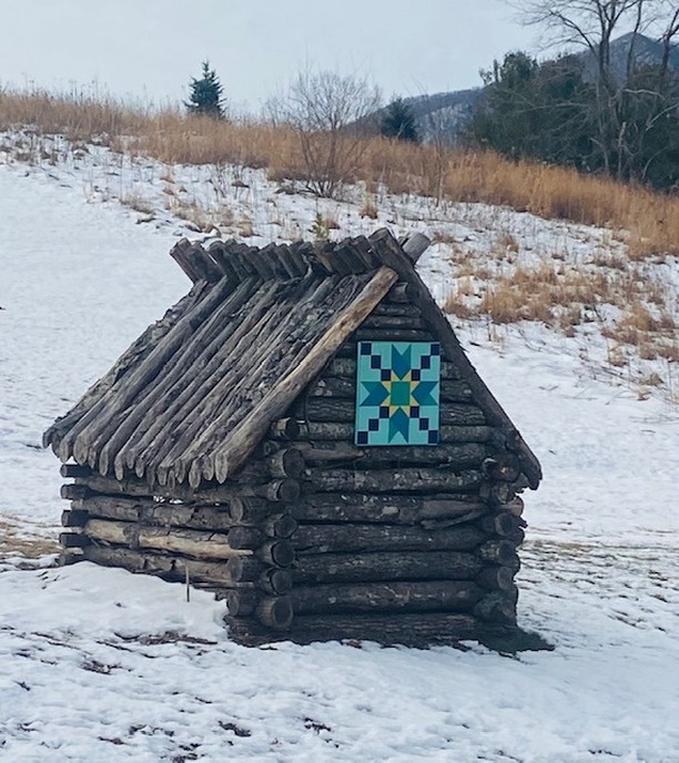 a barn quilt hanging on the small barn covered with snow around.