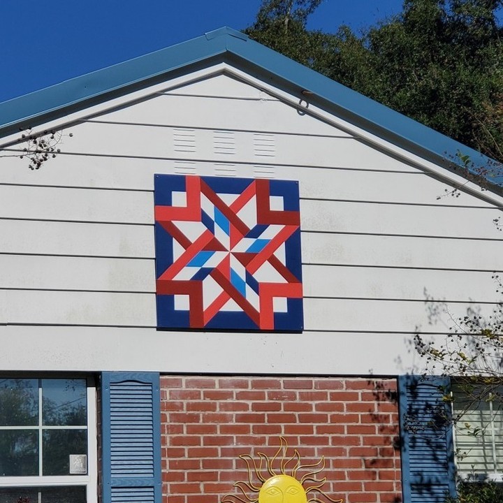 a star pattern barn quilt hanging on the ledge of the house.