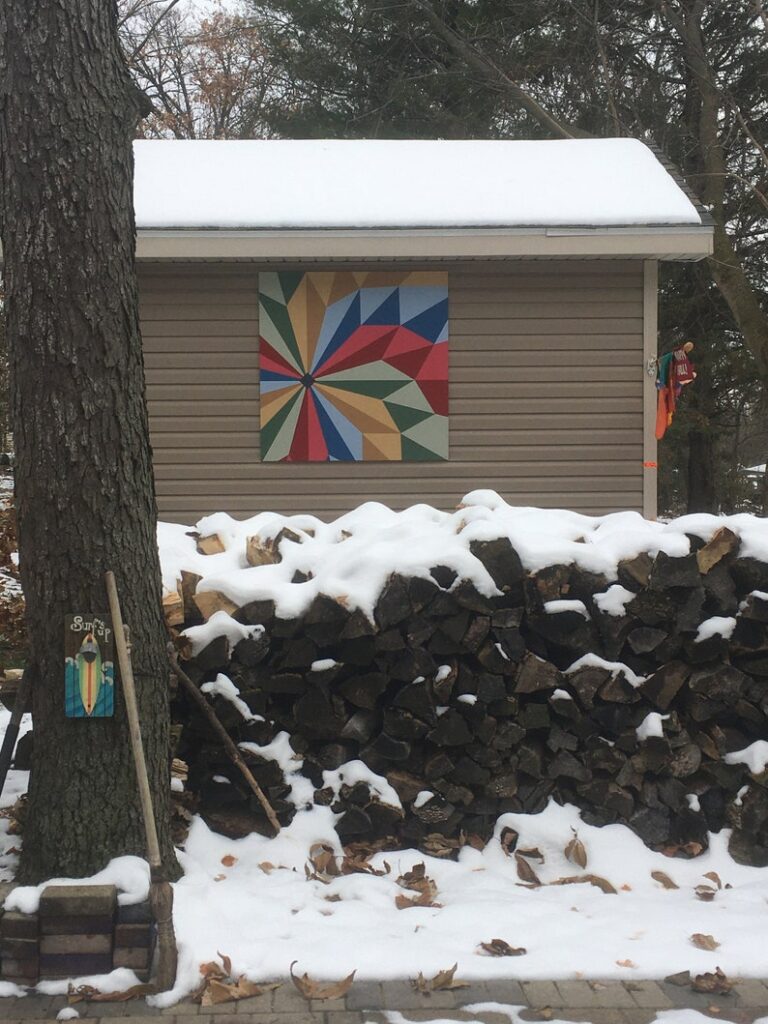 a barn quilt hanging on the barn surrounded by snow.