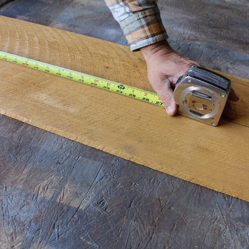 A hand is using a tape measure to measure a wooden board