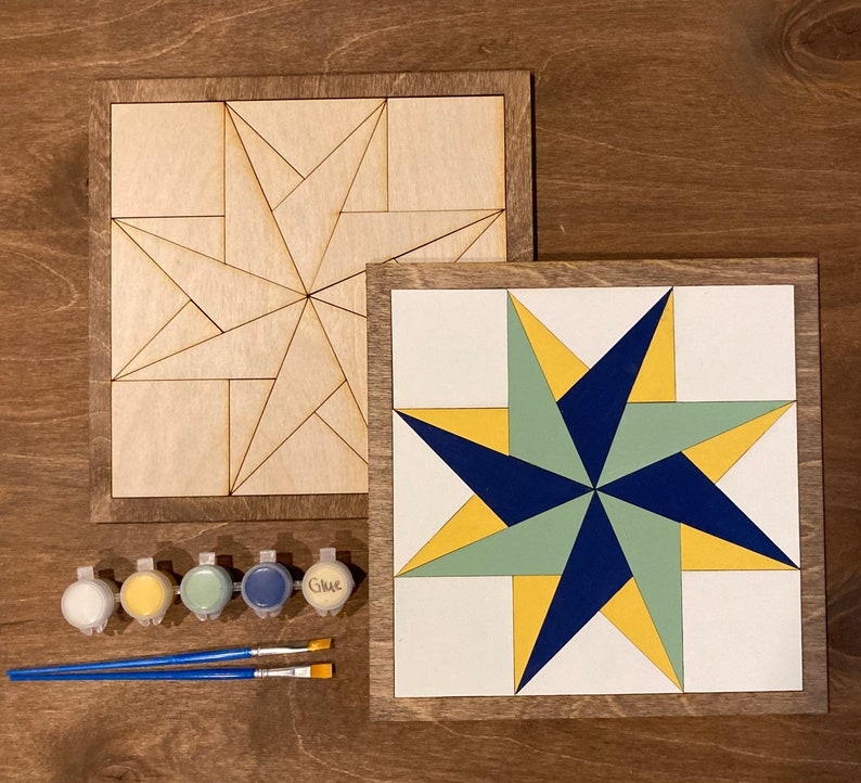 two pinwheel barn quilt laying on the wooden floor, next to five color box and two brush.