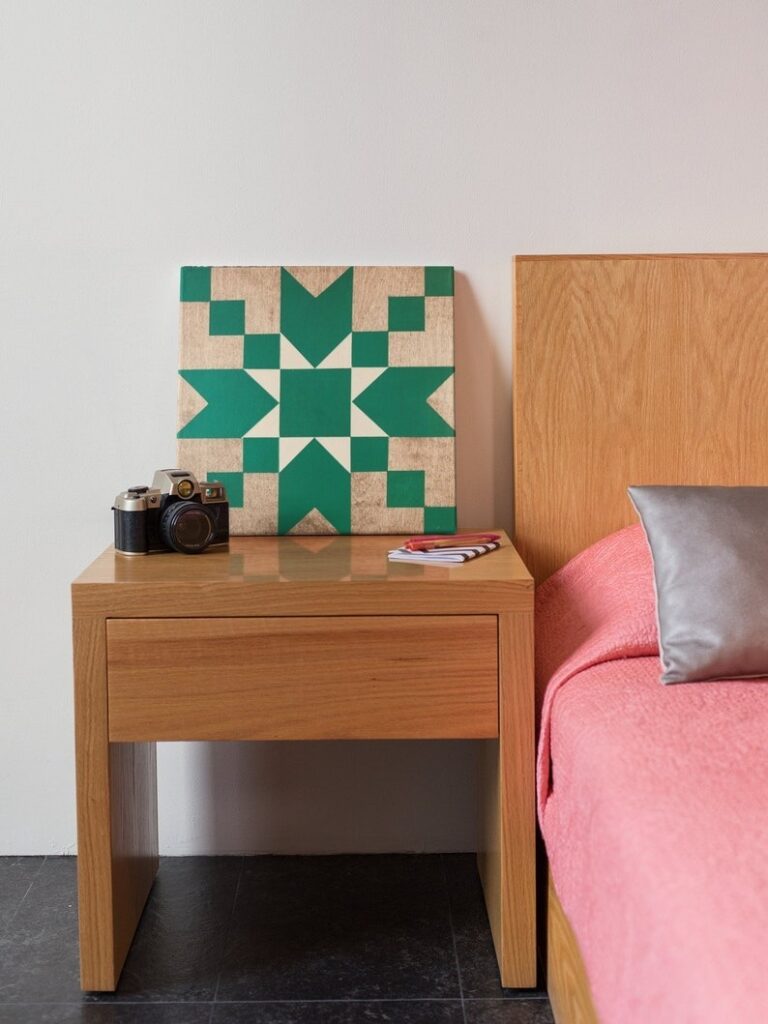 a small barn quilt with the teal star pattern placed on the wooden nightstand, next to the wooden bed.