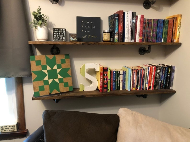 a small barn quilt with a teal star pattern placed on the metal rack on the wooden bookshelf.