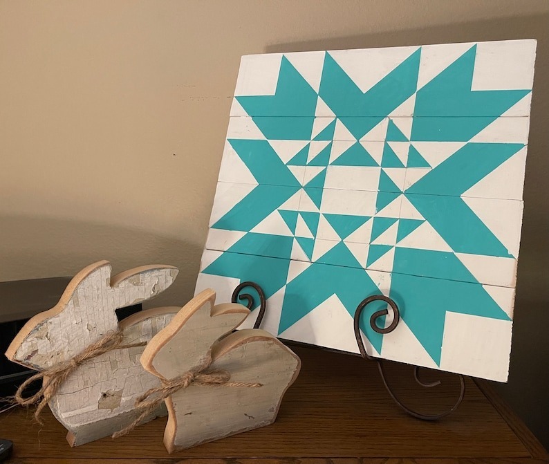 a teal barn quilt placed on the metal rack on the wooden table