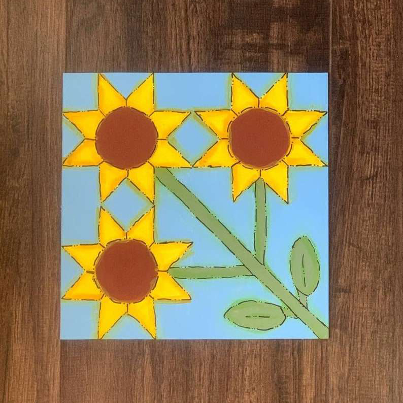 a barn quilt with the 3 sunflowers pattern laying on the wooden floor.