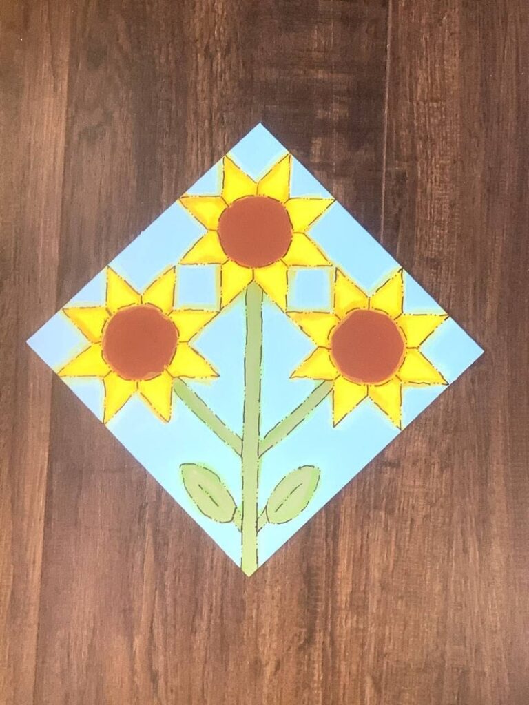 a barn quilt with the 3 sunflowers pattern laying on the wooden floor.