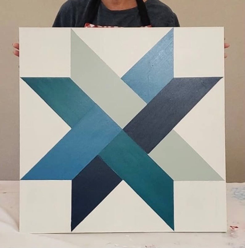 a blue star barn quilt is held by someone with 2 hands.