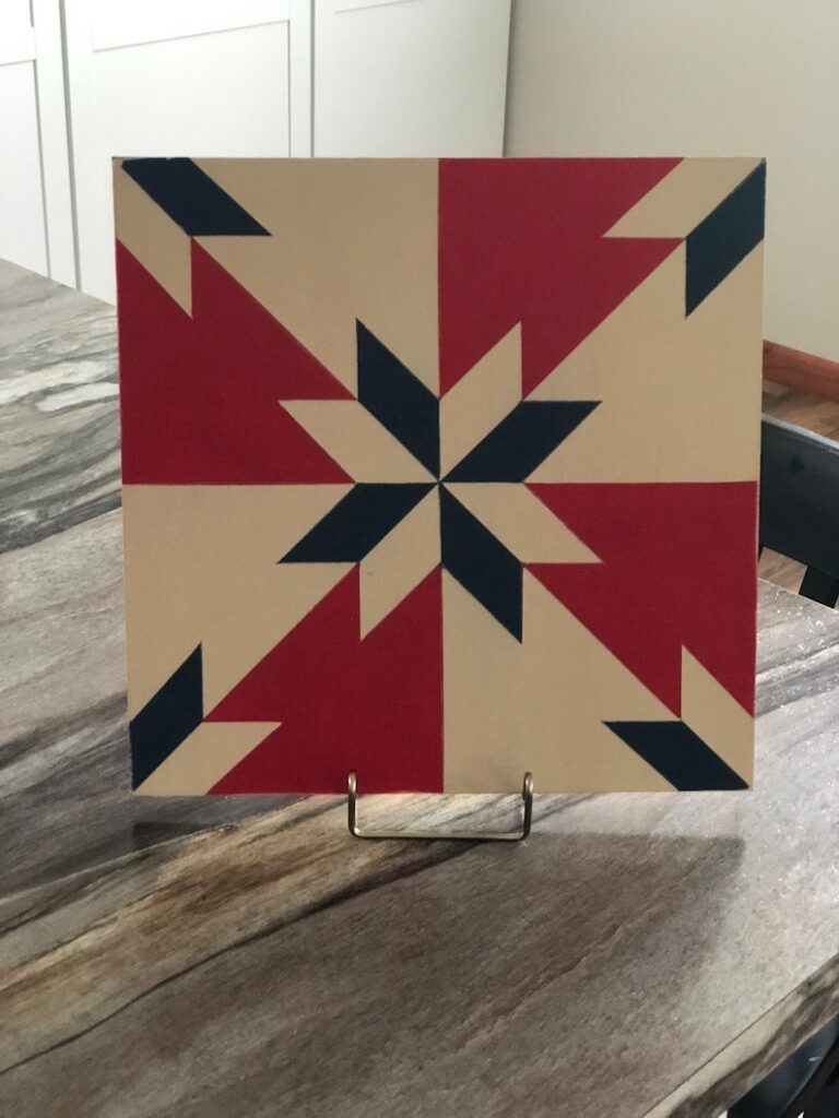 a barn quilt with the color of American Flag placed on the metal rack on the wooden table.