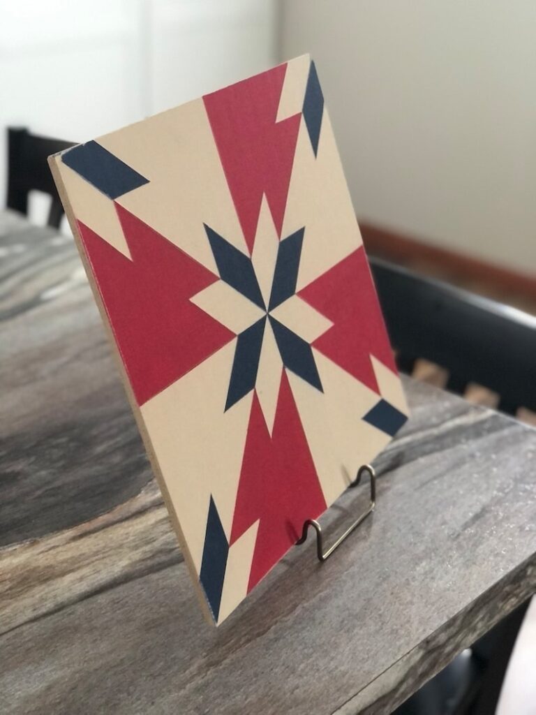 a barn quilt with the color of American Flag placed on the metal rack on the wooden table.