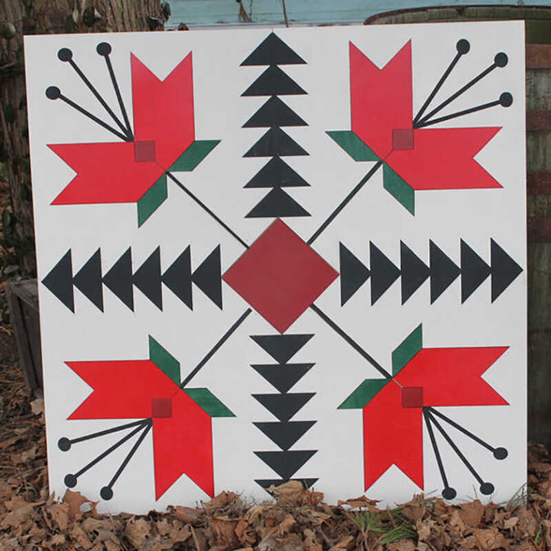 a barn quilt with four red tulips pattern placed in the garden