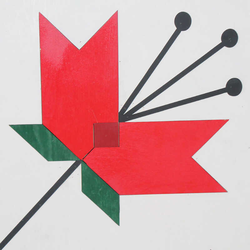 a corner of a barn quilt with four red tulips pattern.