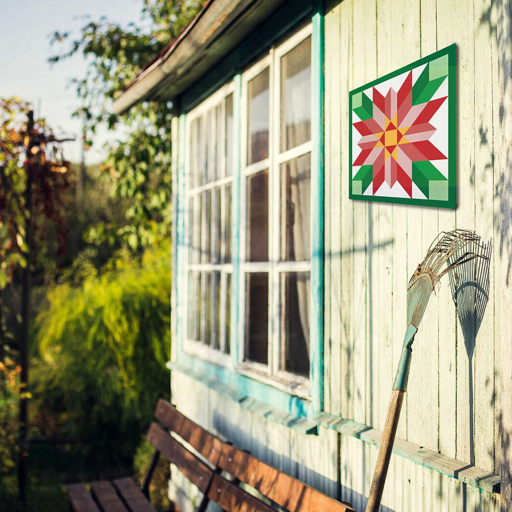 a barn quilt with red flower pattern hanging on the barn