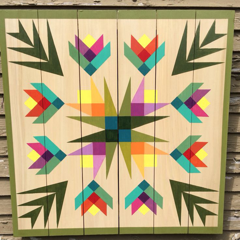 a barn quilt with many small flowers pattern hanging on the wooden wall