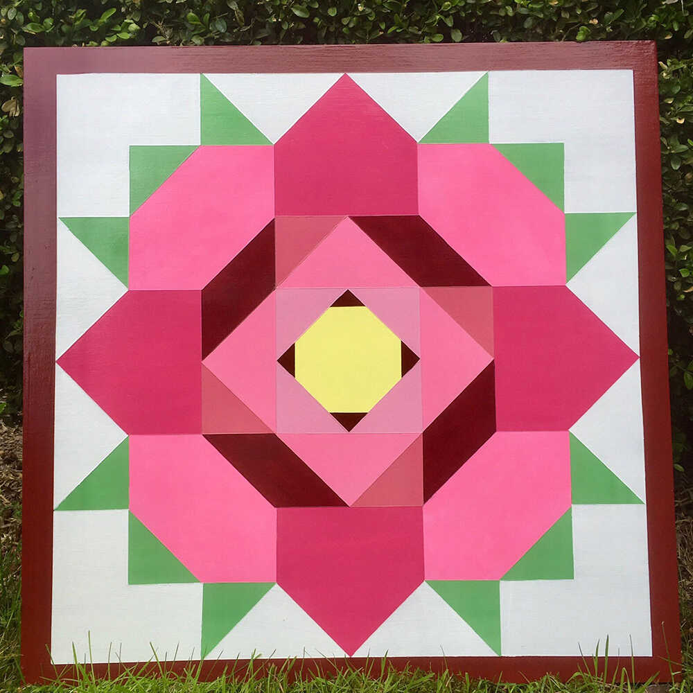 a barn quilt with rose flower pattern placed on the grass in the garden