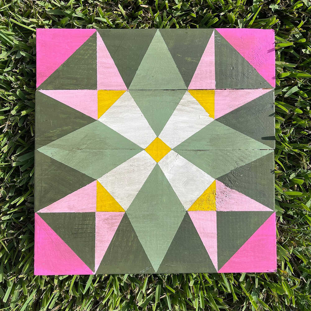 a barn quilt with pink flowers pattern laying on the grass