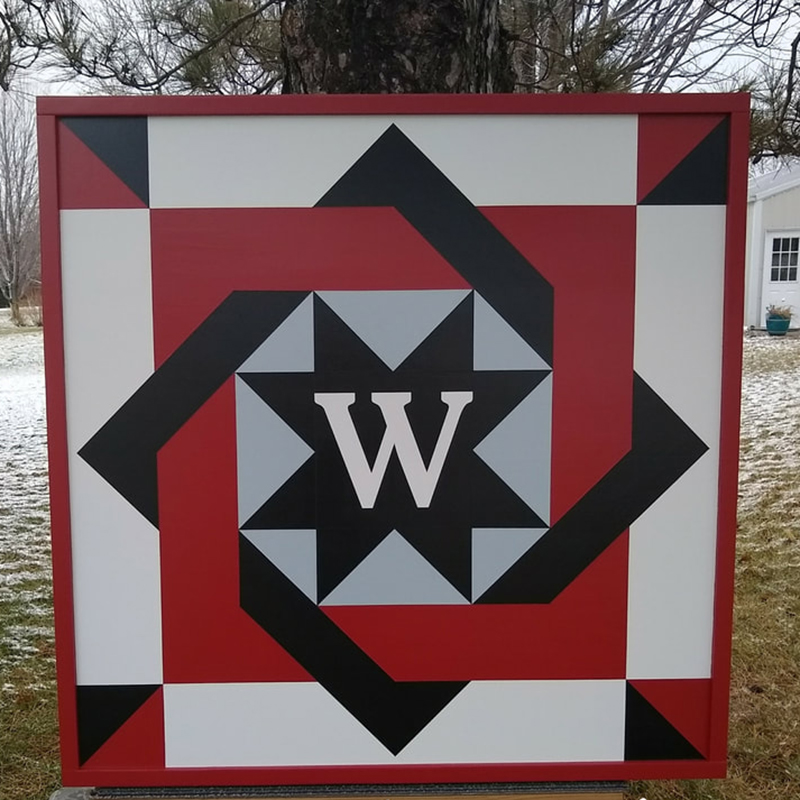 a black and red nested square barn quilt leaning against the tree in the garden