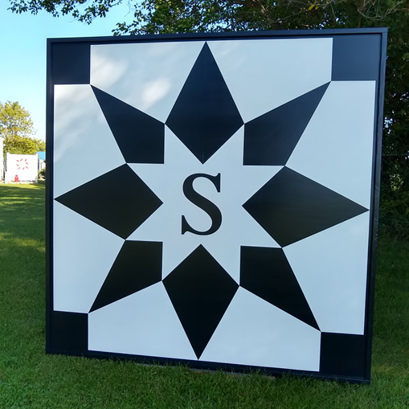a barn quilt with black star placed in the garden