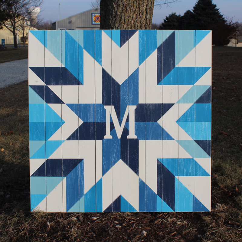a white and blue star barn quilt leaning against the tree in the garden.