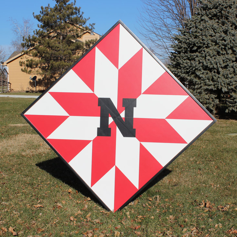 a barn quilt with red geometry pattern placed in the garden