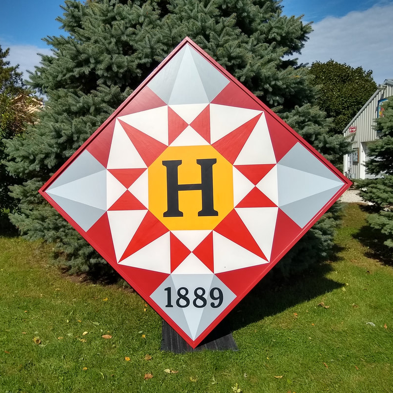 a barn quilt with red star pattern placed in the garden