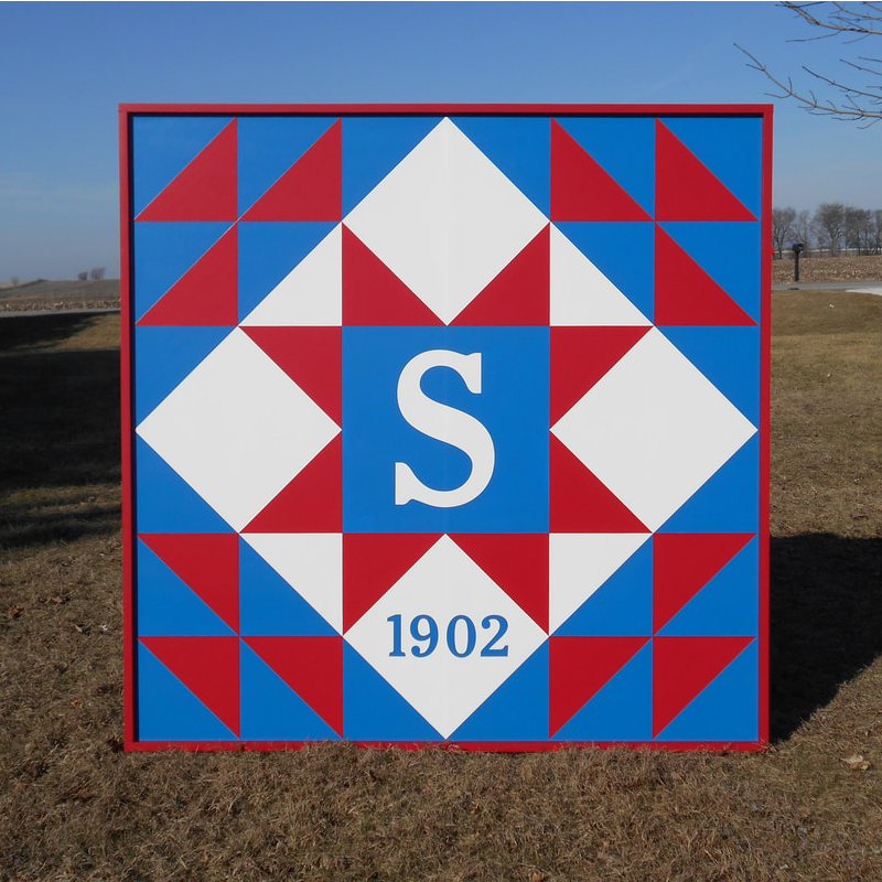 a barn quilt with red triangle and red star pattern placed in the garden