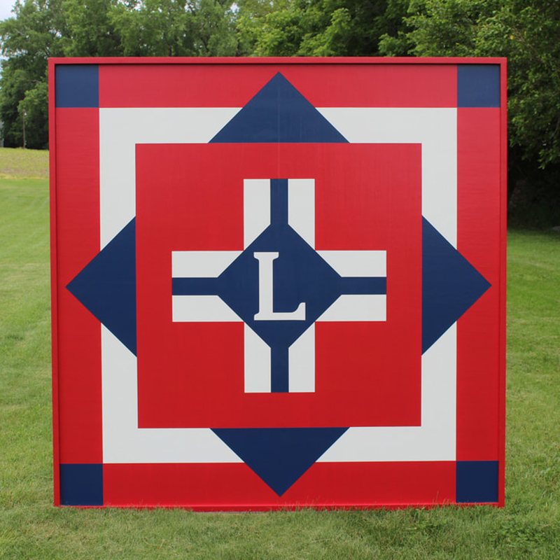 a red barn quilt with plus pattern placed in the garden