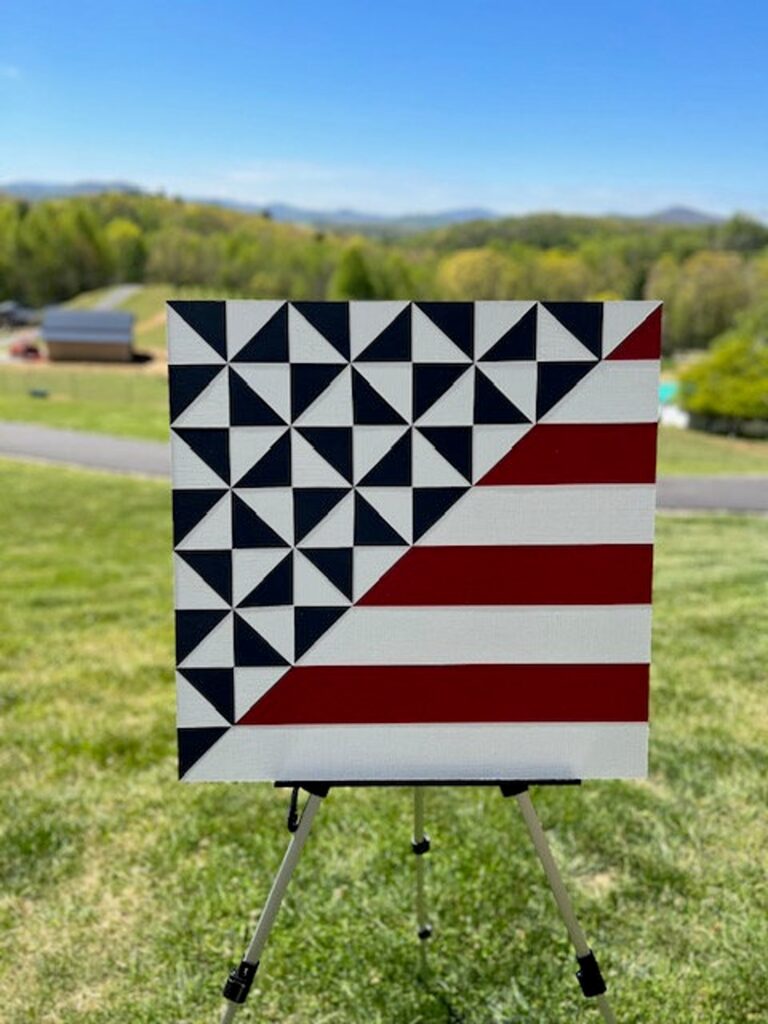 a barn quilt with american flag pattern placed on the metal rack in the garden.