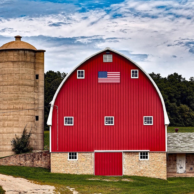 a barn quilt with an American Flag pattern hanging on the red barn.
