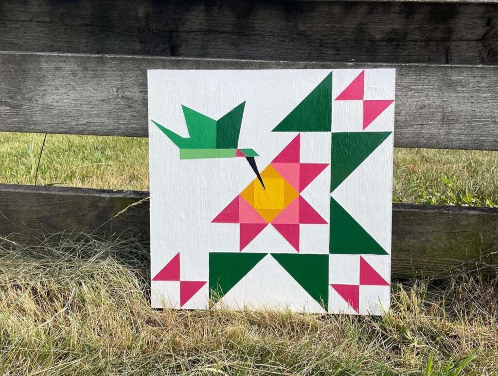 a seagull wing barn quilt placed on the grass, leaning against the wooden fence.