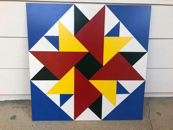 a barn quilt leaning against the wall, on the floor.