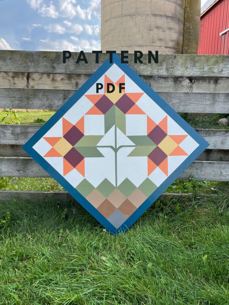a barn quilt placed on the grass, leaning against the wooden fence. Flower pattern