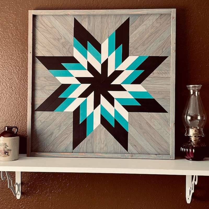 a barn quilt with the colorful star pattern placed on the a white shelf, leaning against red wall.