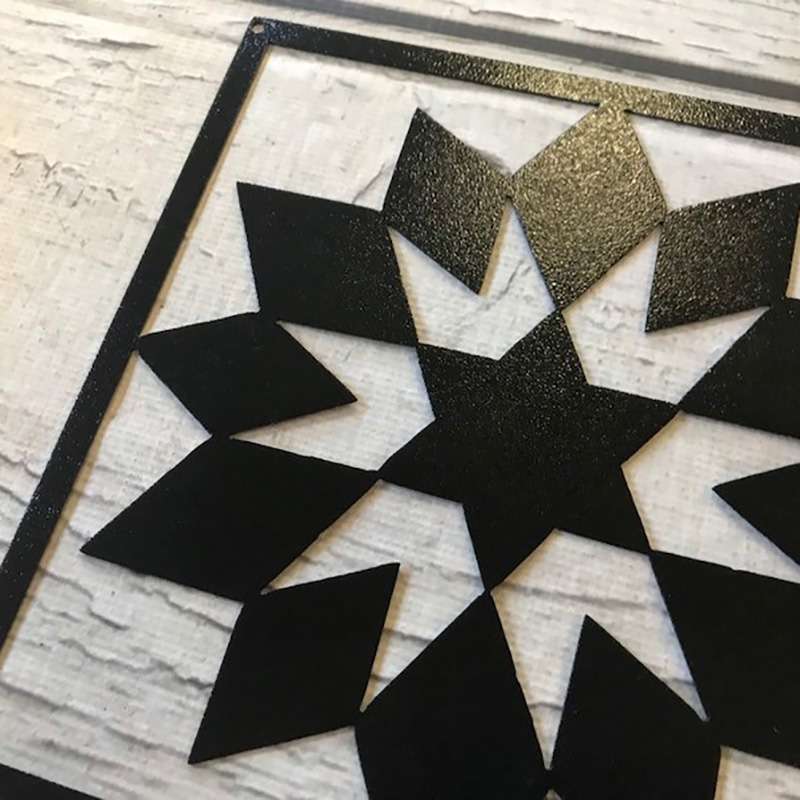 a corner of this barn quilt with black metal star pattern laying on the wooden floor
