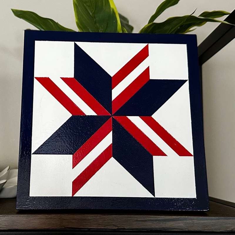 a barn quilt with the American flag star pattern placed on the table, leaning against a tree.