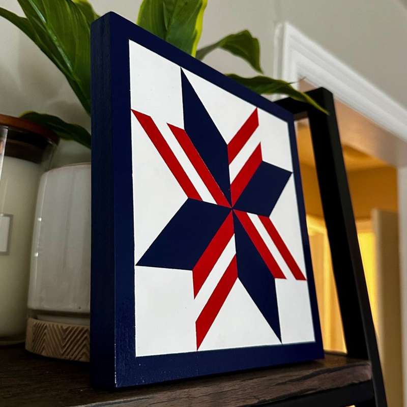 a barn quilt with American flag star pattern placed on the wooden table, leaning against a tree
