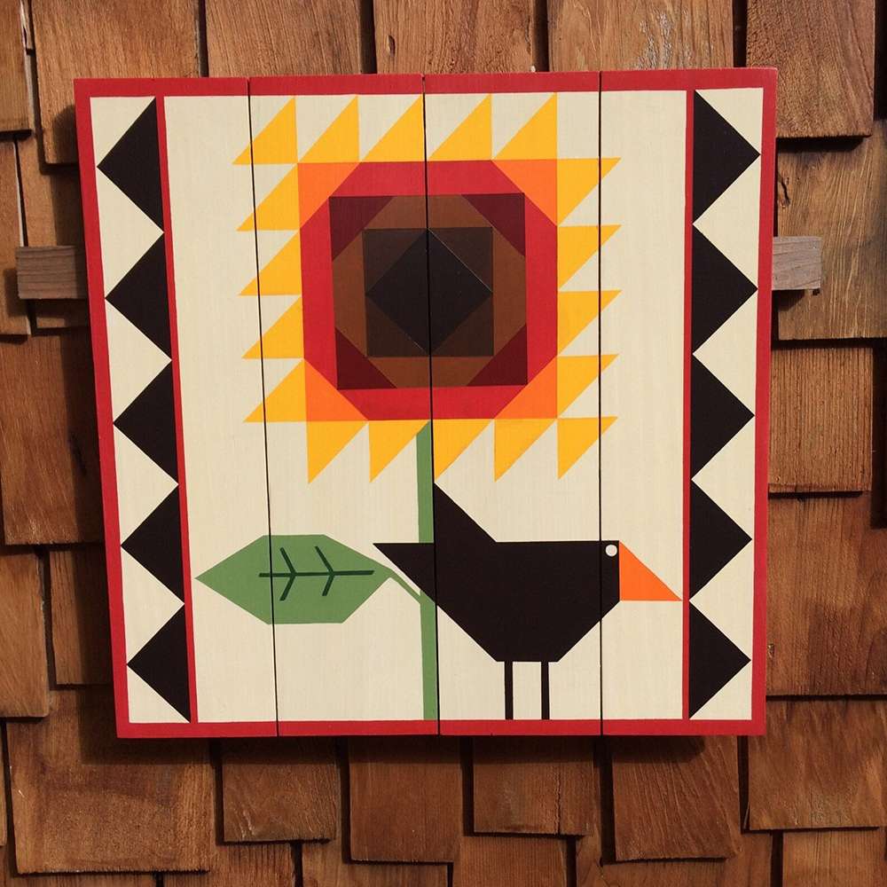 a barn quilt with the crow and sunflower patterns hanging on the wooden wall