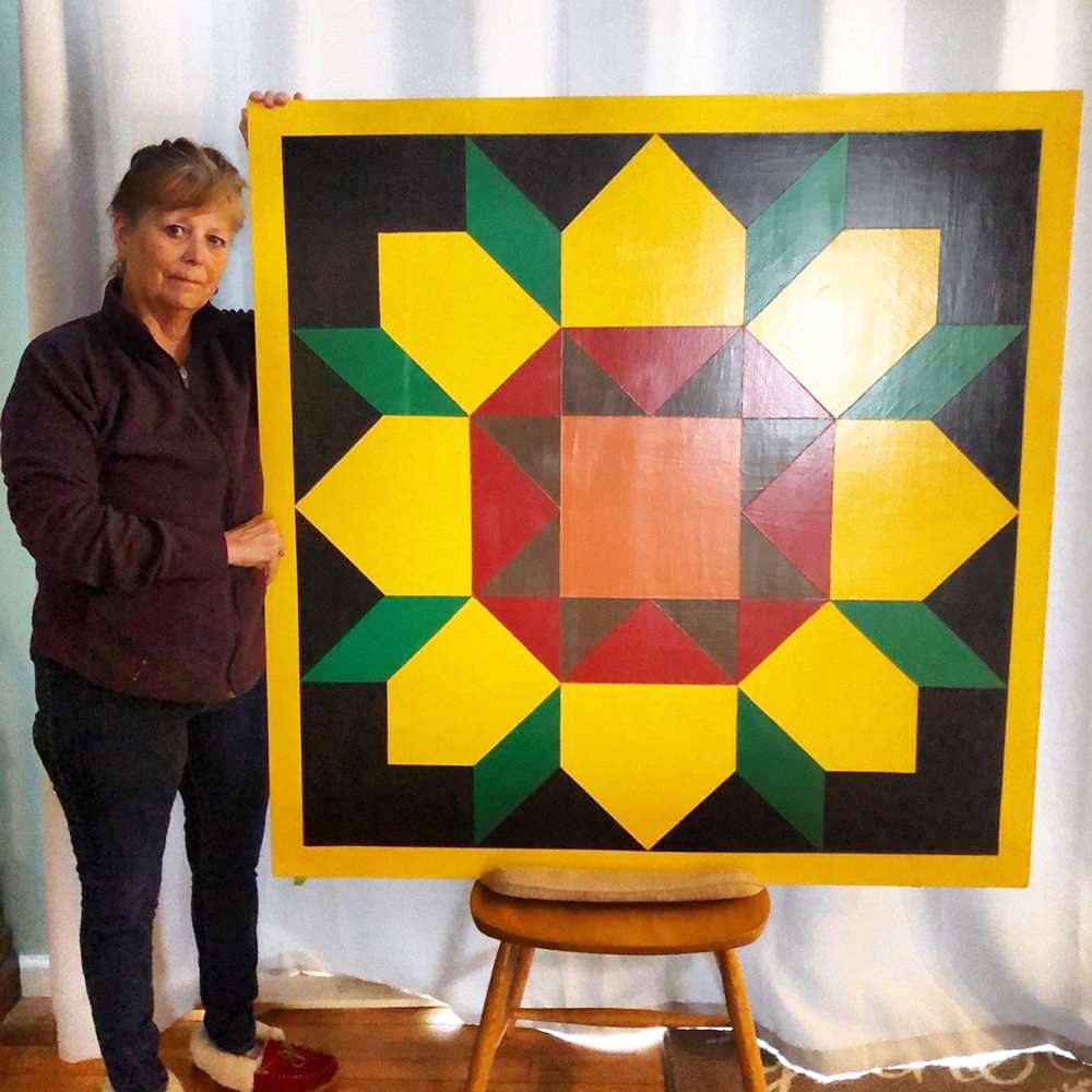 a sunflower barn quilt placed on the wooden chair, next to a woman.
