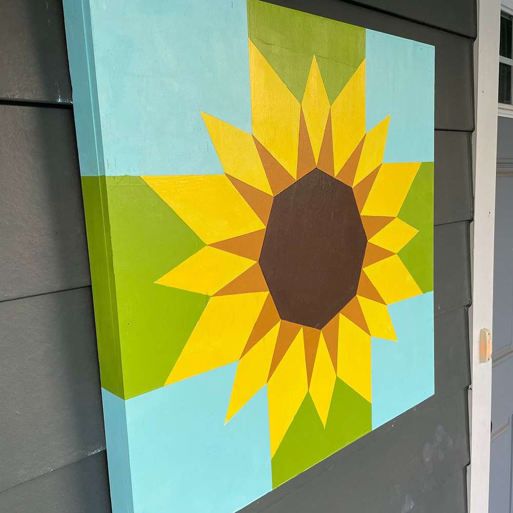a sunflower barn quilt hanging on the gray wall
