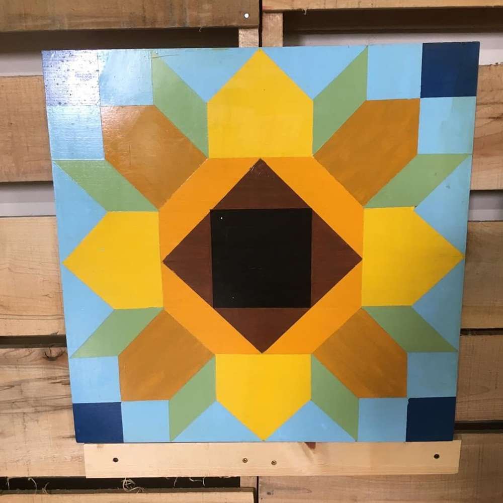 a small sunflower barn quilt hanging on the wooden fence