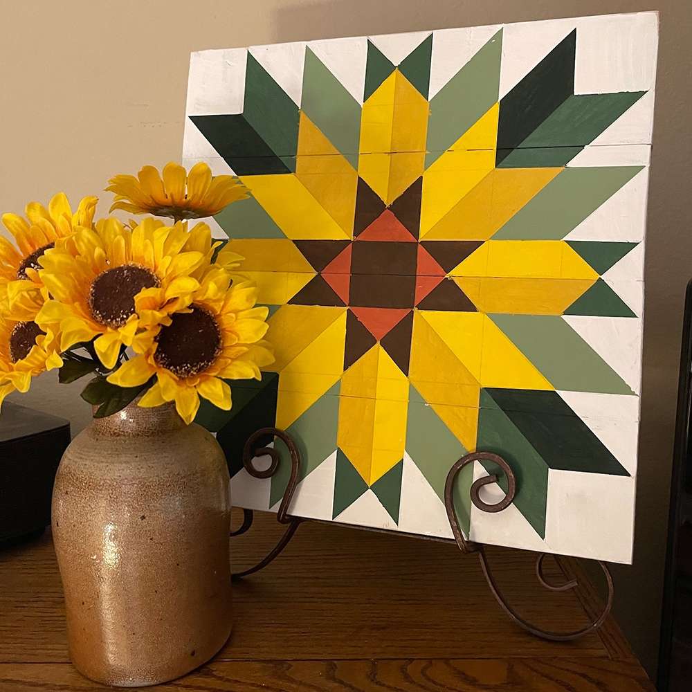 a sunflower barn quilt placed on a metal stand next to a vase of sunflowers