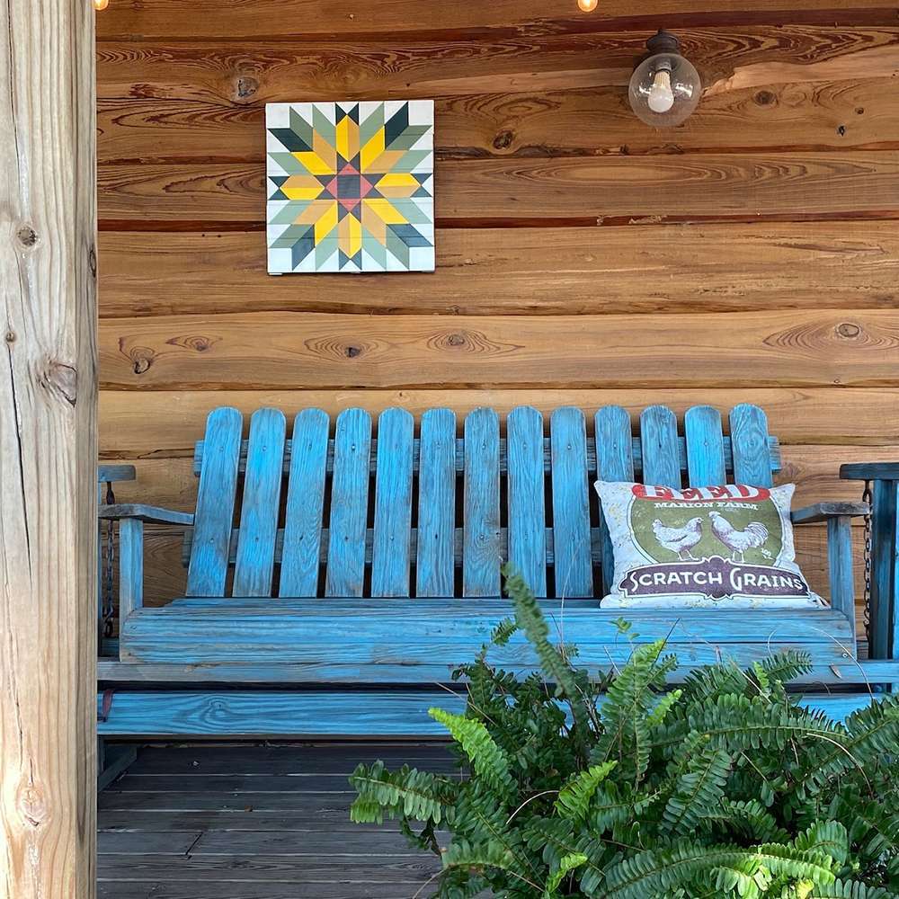 a sunflower barn quilt hanging on the wooden wall, above a blue bench