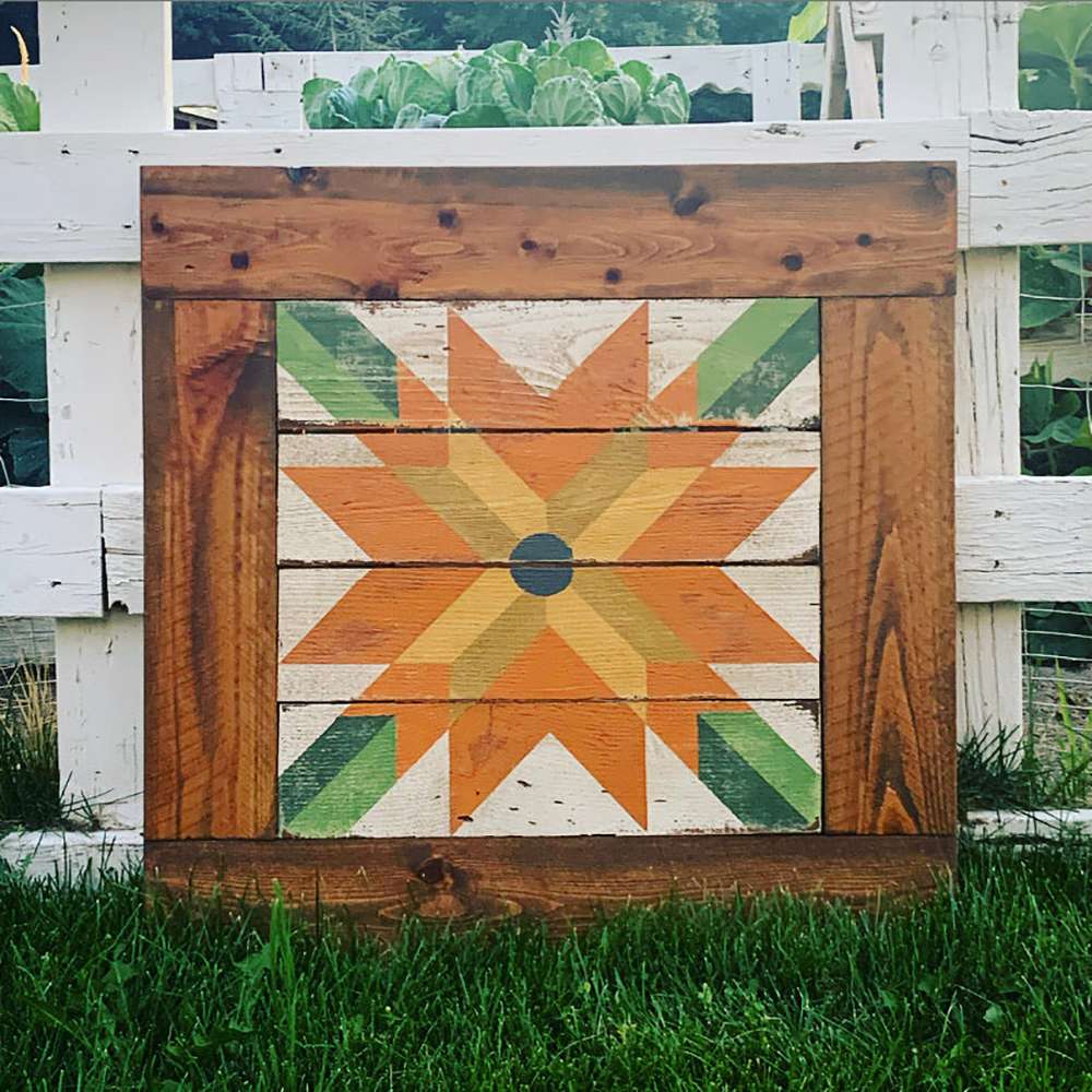 a sunflower barn quilt place on the grass, leaning against the wooden fence