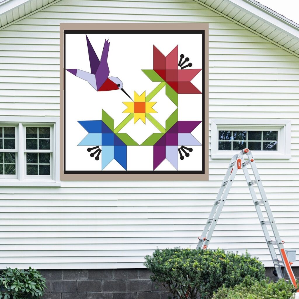 the square barn quilt with hummingbirds in flight pattern hanging on the white wall.