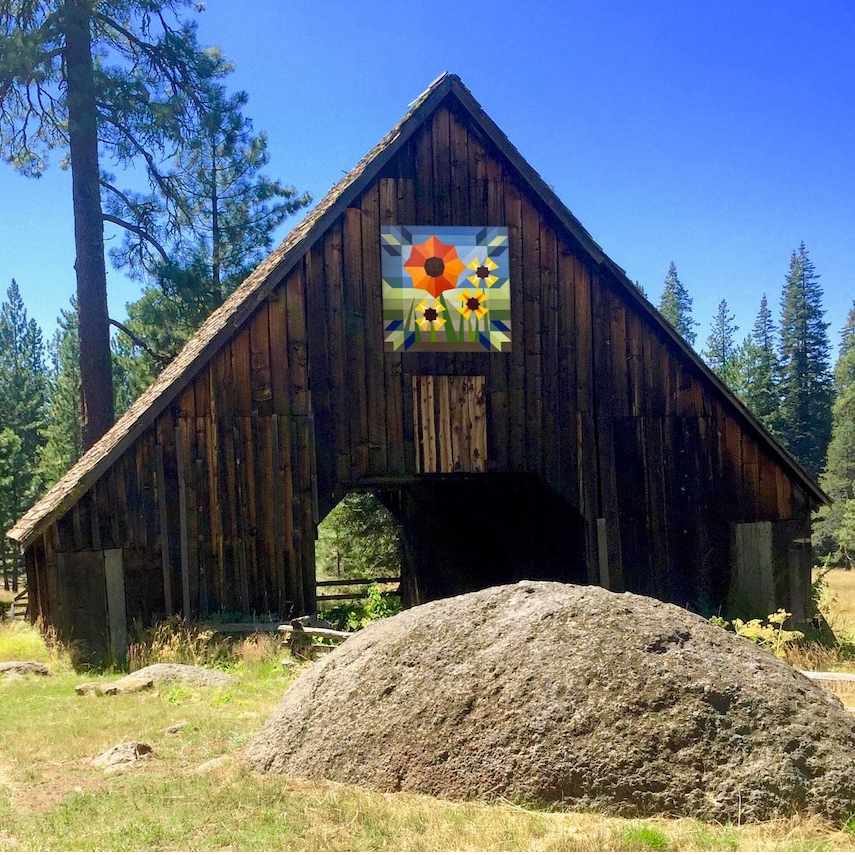 the square barn quilt with brilliant flower patterns hanging on the wooden barn.